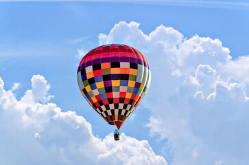 Colorful hot air balloon flying over blue sky with white clouds