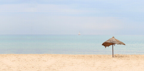 Banner of the seascape. Straw beach umbrella on a tropical sandy beach on a background of blue sea on a sunny day. Idyllic travel and summer vacation concept