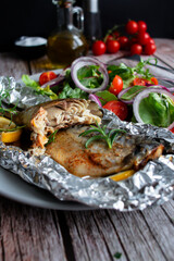 Mackerel baked in foil with vegetables on a plate. on a wooden background
