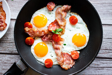 Fried eggs with bacon and fresh tomatoes. On a wooden background