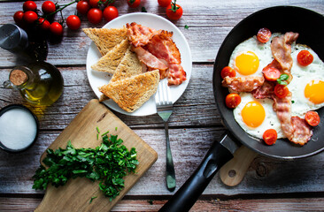 Fototapeta na wymiar Fried eggs with bacon and fresh tomatoes. On a wooden background