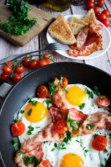 Fried eggs with bacon and fresh tomatoes. On a wooden background