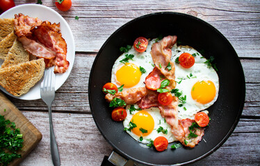 Fried eggs with bacon and fresh tomatoes. On a wooden background