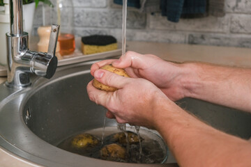 A man washes a potato from ground under a stream of tap water for further cooking. Preparation of potatoes for peeling. Cleaning peel from pesticides. A man cooks dinner or lunch at home for family.