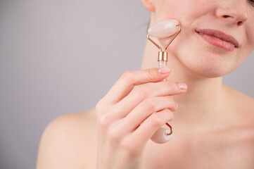 Close-up portrait of a woman using a quartz roller massager on her cheek for an alternative...