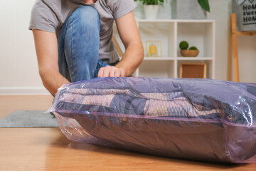 A man folds winter jackets and puts them in a vacuum bag for seasonal storage in the closet.