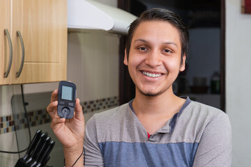 Young diabetic man holding blood sugar meter. Checking Blood Sugar Level At Home. Diabetic Checking Blood Sugar Levels. Checking blood sugar level by glucometer and test stripe at home
