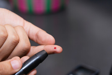 Young Latino man doing blood sugar test in the kitchen. Blood glucose test. Drawing blood for medical test. Using glucose meter in the kitchen.