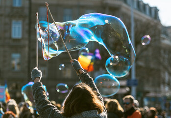 A group of people are creating huge, bright soap bubbles in mid-air with a bubble wand, marveling...