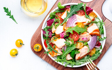 fresh salad with grilled salmon with tomato, cucumber, arugula, radicchio, red onion and lettuce with lemon oil dressing. Healthy delicious lunch. White table background, top view