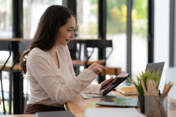 Obraz premium An Asian businesswoman using a digital tablet while sitting at a work desk in an office