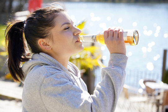 Woman on vacation or leisure drinking beer or lemonade from a glass bottle by a lake on a sunny day in summer