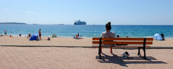Cote d'Azur in Frankreich Sandstrand mit Frau und Hund auf Bank, Kreuzfahrtschiff im Hintergrund...