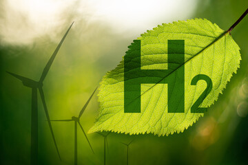 Formula of hydrogen on a green leaf. Wind turbines on a background. Green hydrogen concept