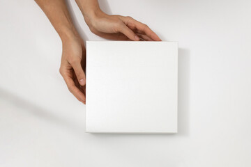 Mockup of white box on white background. Hands holding blank cardboard gift
