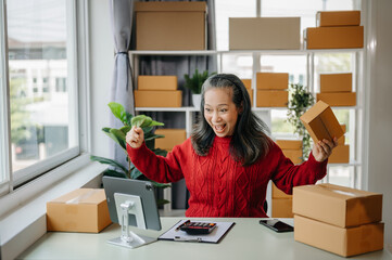 Senior business owner woman prepare parcel box and standing check online orders for deliver to customer on tablet, laptop Shopping Online concept. at home office.