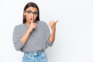 Young caucasian woman isolated on white background pointing to the side and doing silence gesture