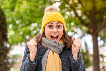 Brunette woman wearing winter jacket at outdoors celebrating a victory in winner position