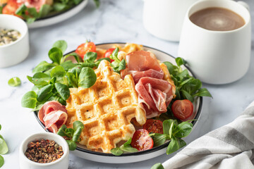 Cheesy belgian waffles served with ham, tomatoes and lettuce corn on white marble background . Savory waffles. Healthy breakfast