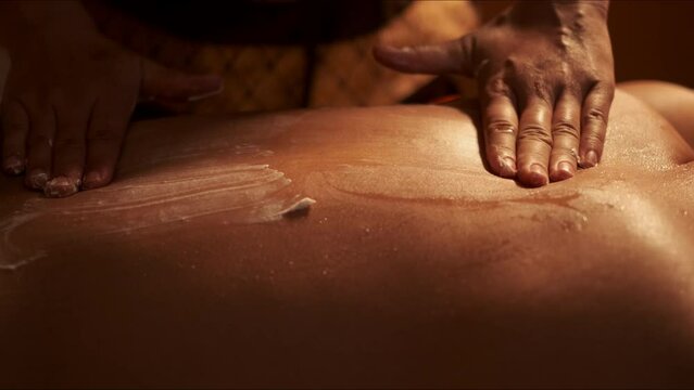 Masseuse hand applying cream scrub on back skin of a man customer in spa salon.