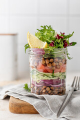 Healthy Homemade Mason Jar Salad with lentils and vegetables with fork on kitchen table close up. Healthy food, Diet, Detox, Clean Eating or Vegetarian concept