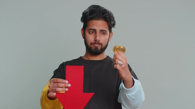 Upset indian man showing red arrow pointing down, downgrade, unsuccessful business, fall of cryptocurrency stock market investment, mining bitcoins BTC money exchange rate, bankruptcy fail. Hindu guy