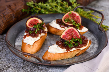 Canape or crostini with toasted baguette, cream cheese, onion jam, figs and fresh thyme on a tin tray. Ideal appetizer as an aperitif.
