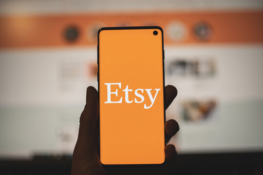 Man holding a smartphone with Etsy app orange logo with blurred website as background. SWANSEA, UK - MARCH 19, 2021