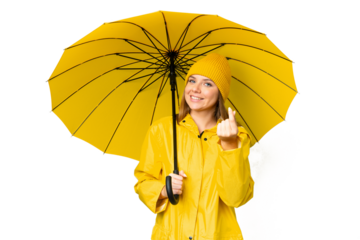 Young blonde woman with rainproof coat and umbrella over isolated chroma key background making money gesture