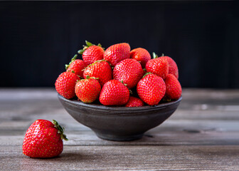 Ripe garden strawberries in a vase on a wooden table.