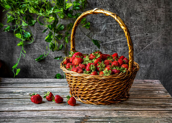 Fototapeta na wymiar Basket with strawberries on a wooden table against the backdrop of a stone wall.