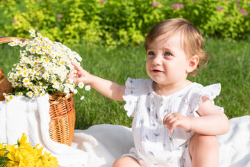 Cute little baby on picnic with flowers and fruits in the summer park, sunny day