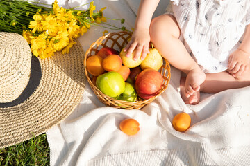 close up baby hand takes organic fruits, straw hat, flowers, sunny day