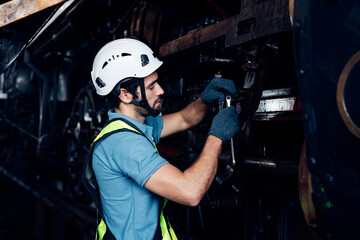 Male engineer maintenance locomotive engine wearing safety uniform, helmet and gloves work in locomotive repair garage. 