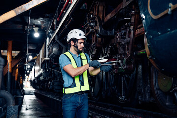 Male engineer maintenance locomotive engine wearing safety uniform, helmet and gloves work in locomotive repair garage. 