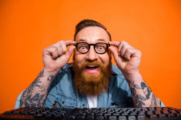 Photo of astonished positive person arms touch eyeglasses computer keyboard isolated on orange color background