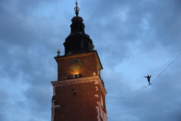 Tightrope walker performing approaching clock tower. Dark sky background.