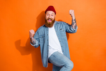 Photo of young funky guy red beard yelling celebrate victory his football club fan fists up wear denim shirt isolated on orange color background
