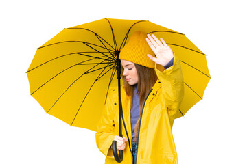 Young pretty woman with rainproof coat and umbrella over isolated chroma key background making stop gesture and disappointed