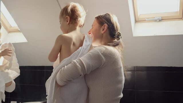 Cute baby boy covered in bath towel with mother looking in his reflection in mirror. Concept of parenting, happiness and child hygiene