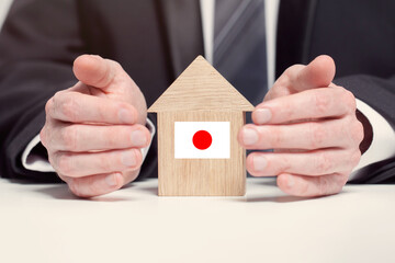 Businessman hand holding wooden home model with Japanese flag. insurance and property concepts