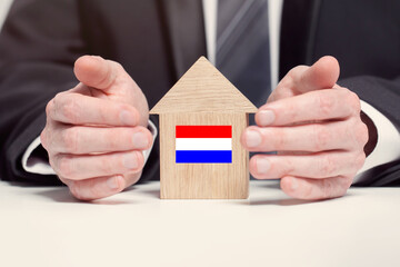 Businessman hand holding wooden home model with Dutch flag. insurance and property concepts