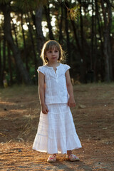 Portrait of  brunette child girl in white clothes standing in the park
