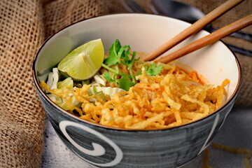 Northern Style Curried Noodle Soup with Chicken, khaao saawy gai, Khao Soi served in a blue cave. on a white table in thailand..