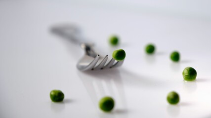 Closeup shot of green peas and a fork isolated on a white background.