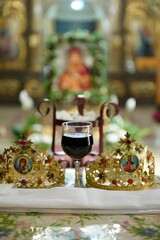 Vertical shot of the ceremonial crowns and a glass of wine as orthodox wedding accessories.