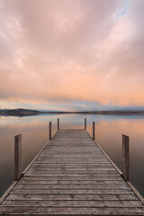 Fototapeta na wymiar Vertical shot of a pier and a scenic seascape at sunset in Zug, Switzerland