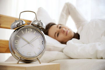Alarm Clock in front of a woman in sleepwear enjoying to sleep in bed on vacation or weekend on a sunny summer morning
