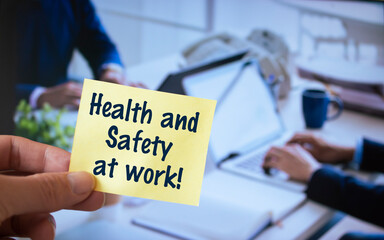 Male hand holding sticky note written Health and Safety at Work.