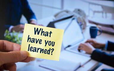 Male hand holding sticky note written What have you learned?
